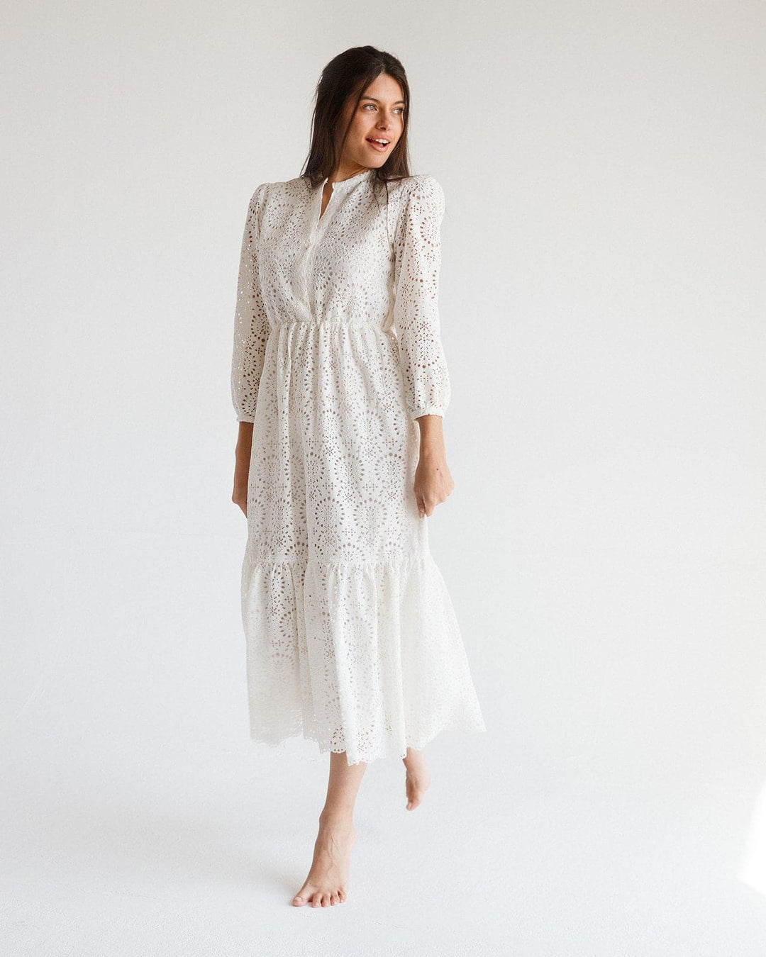 Woman wearing a white eyelet lace midi dress with long sleeves in a minimalist studio.