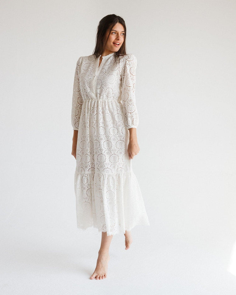 Woman wearing a white eyelet lace midi dress with long sleeves in a minimalist studio.