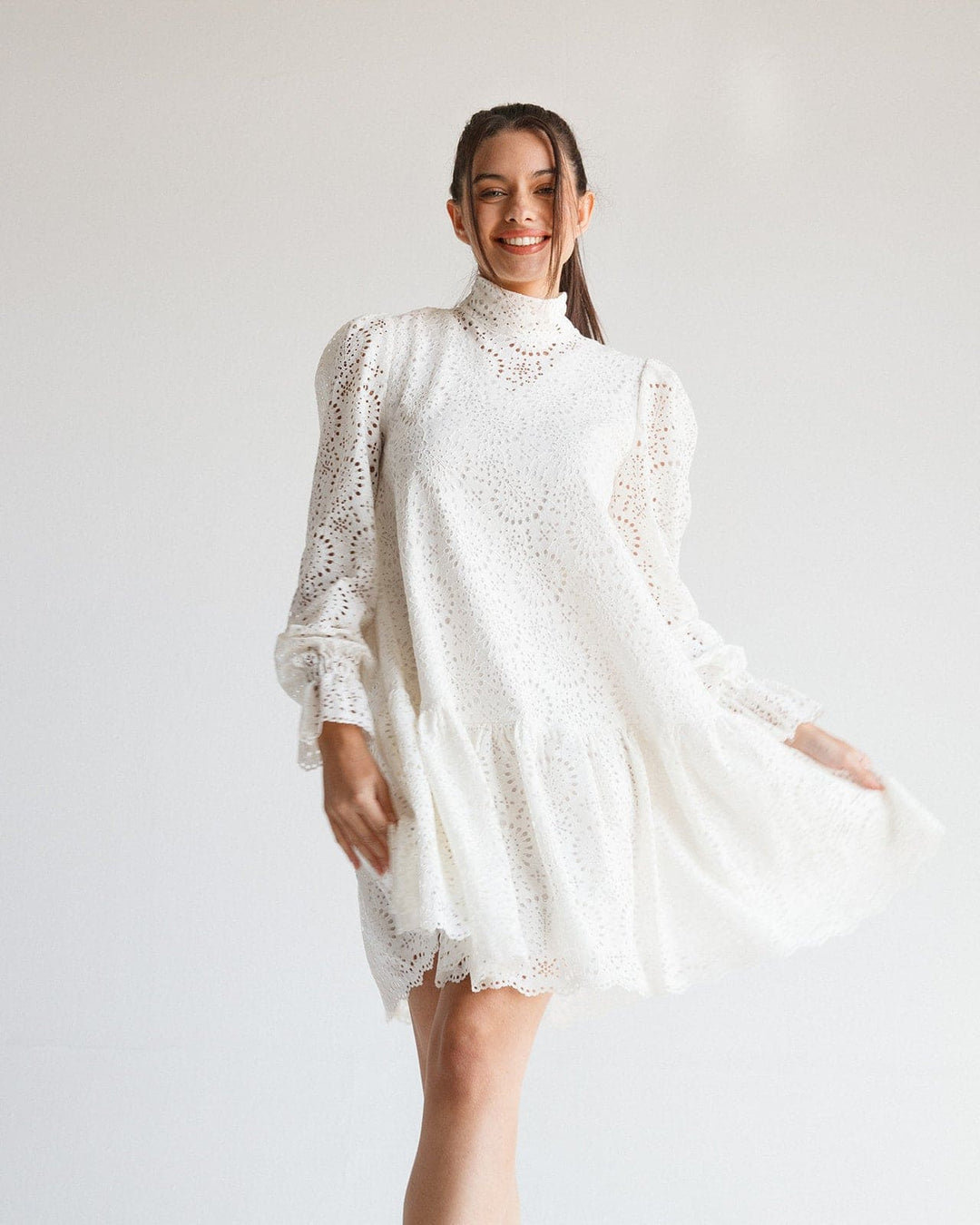 Woman wearing a white lace long-sleeve dress with high neck and ruffled hem in studio