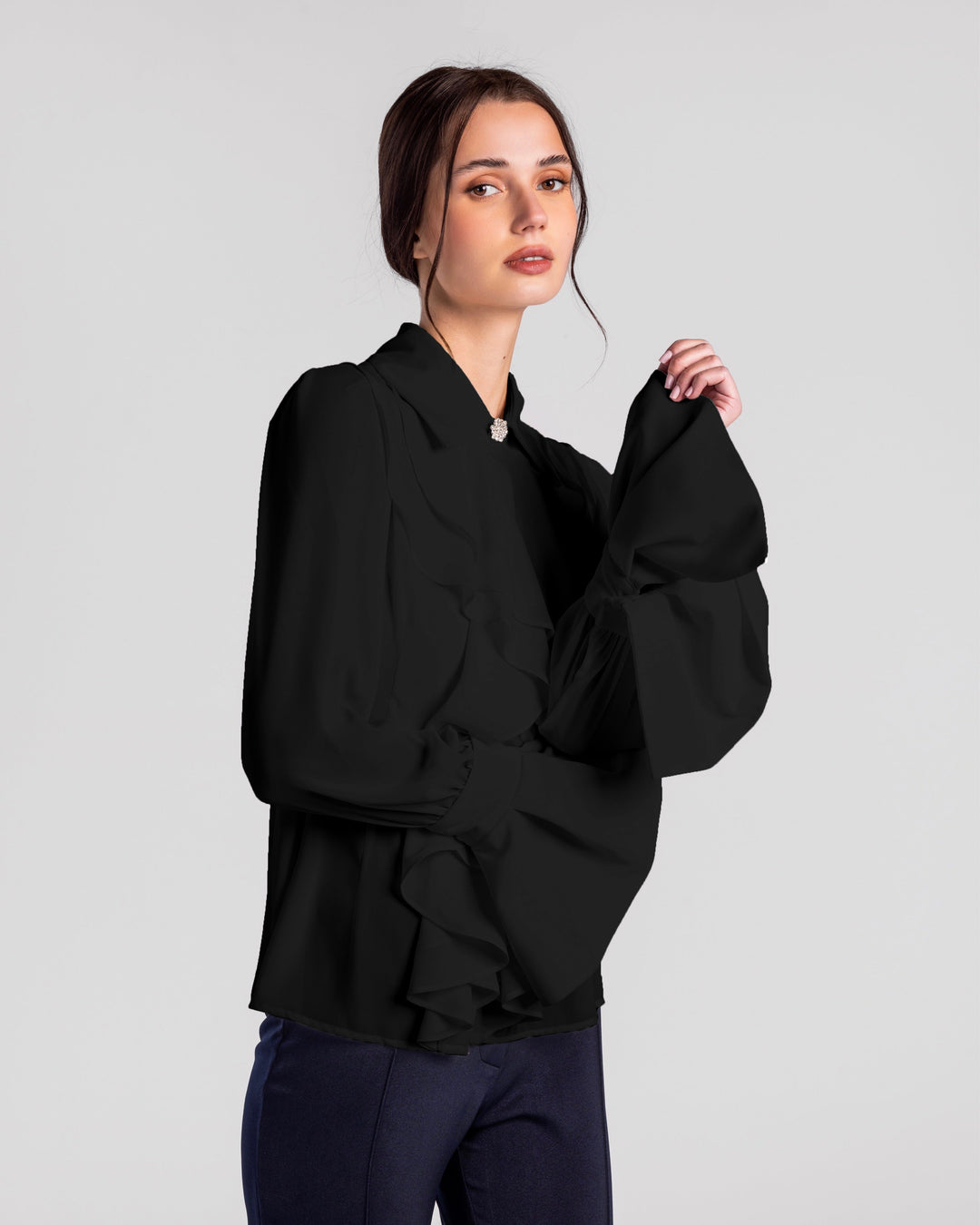 Woman in elegant black ruffled long-sleeve blouse and navy trousers on plain background