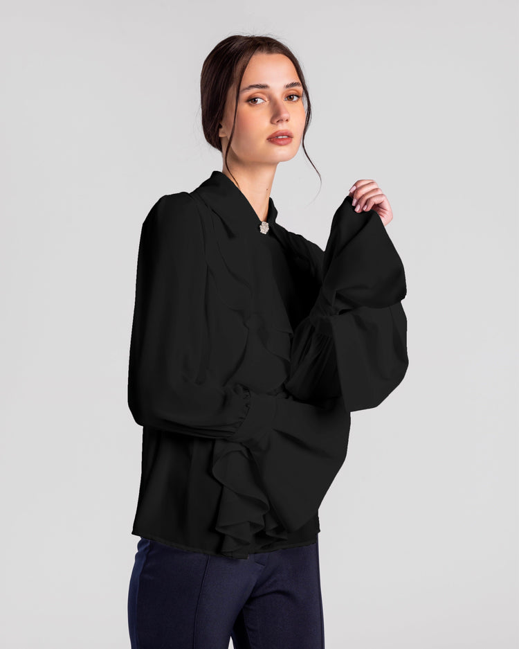 Woman in elegant black ruffled long-sleeve blouse and navy trousers on plain background
