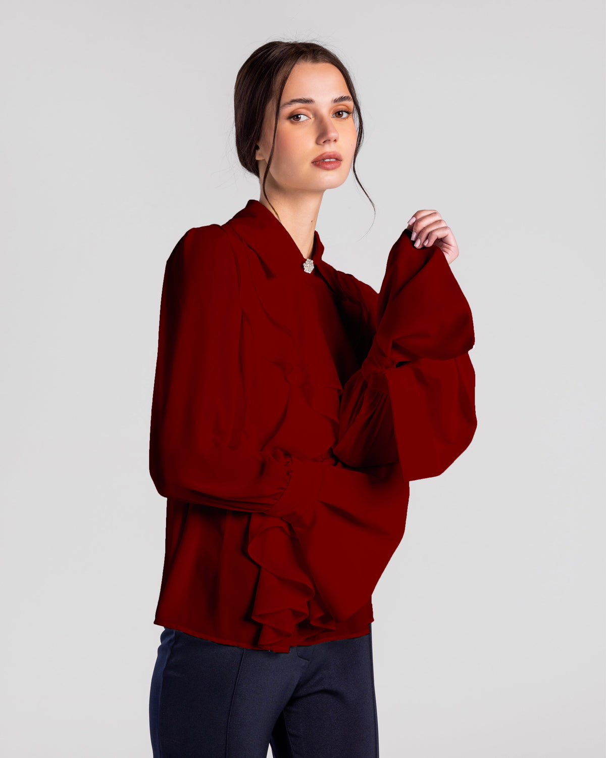 Woman wearing elegant ruffled long sleeve red blouse and dark pants on light background