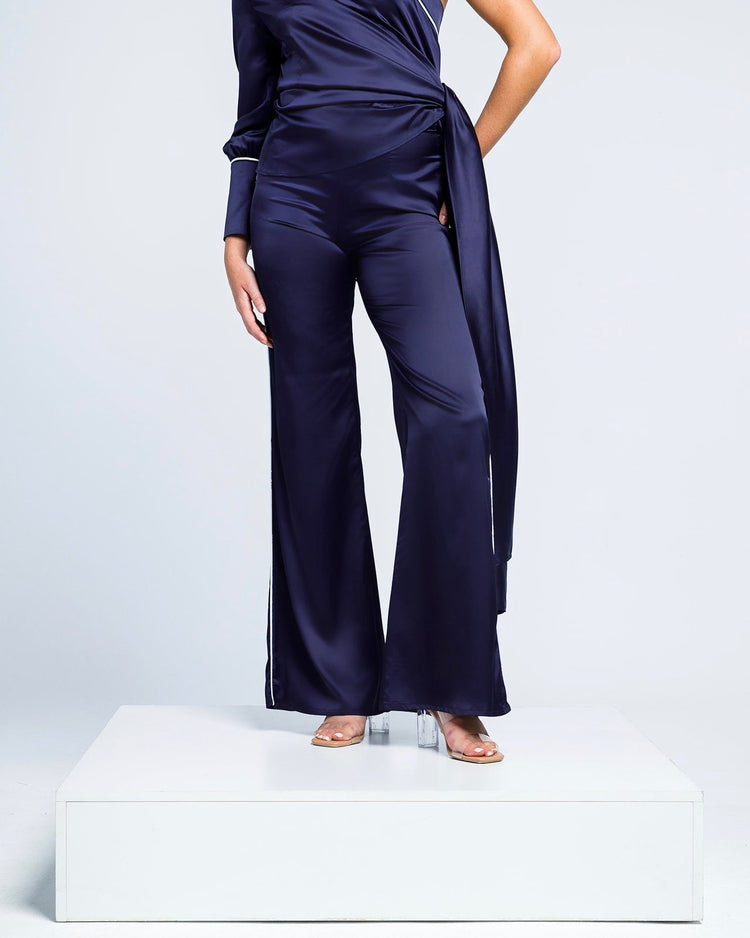 Woman wearing elegant navy satin one-shoulder jumpsuit with flared legs and sash detail