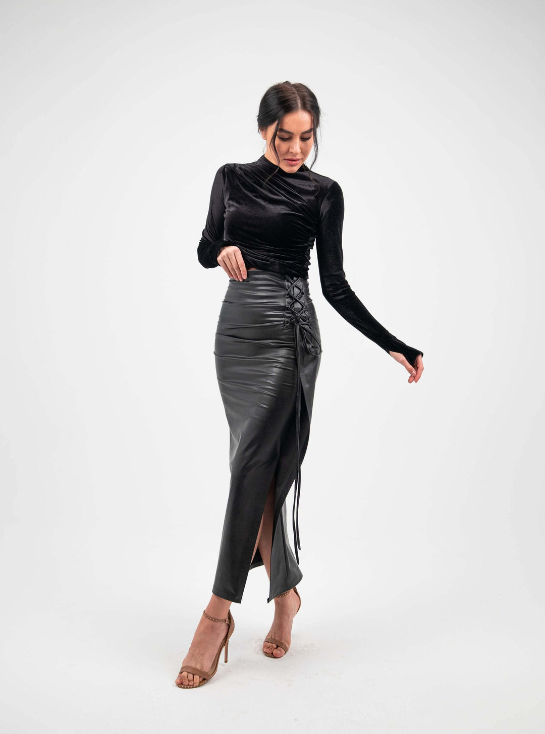 Woman in elegant black velvet top and high-waisted leather skirt with side slit, heels