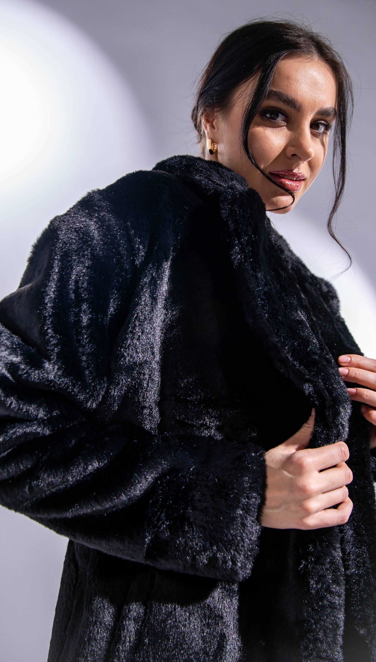 Woman in elegant black faux fur coat with gold hoop earrings, fashion photoshoot