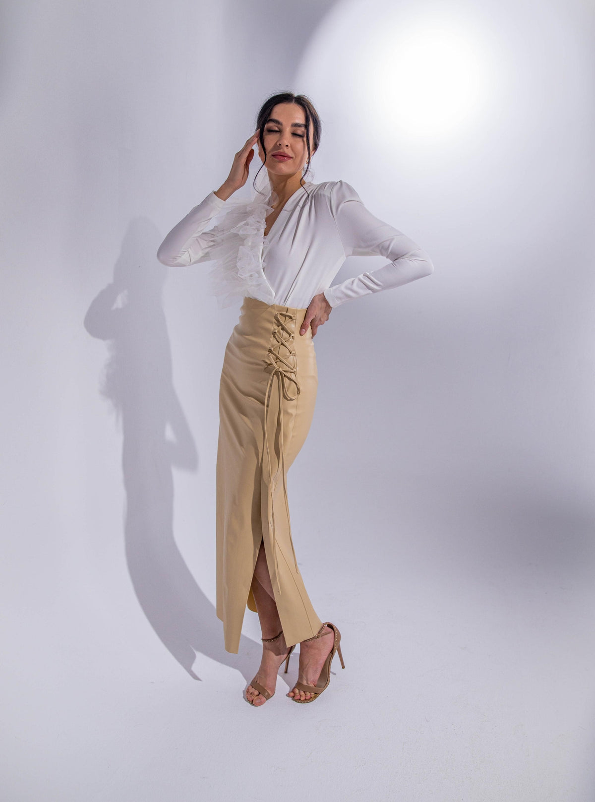 Woman wearing elegant white ruffle blouse and beige lace-up midi skirt in studio setting