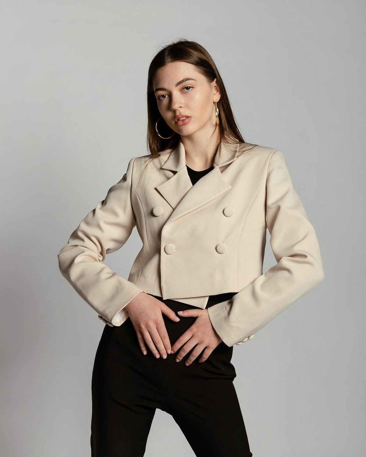 Woman wearing a beige double-breasted cropped blazer and black pants, fashion studio shot