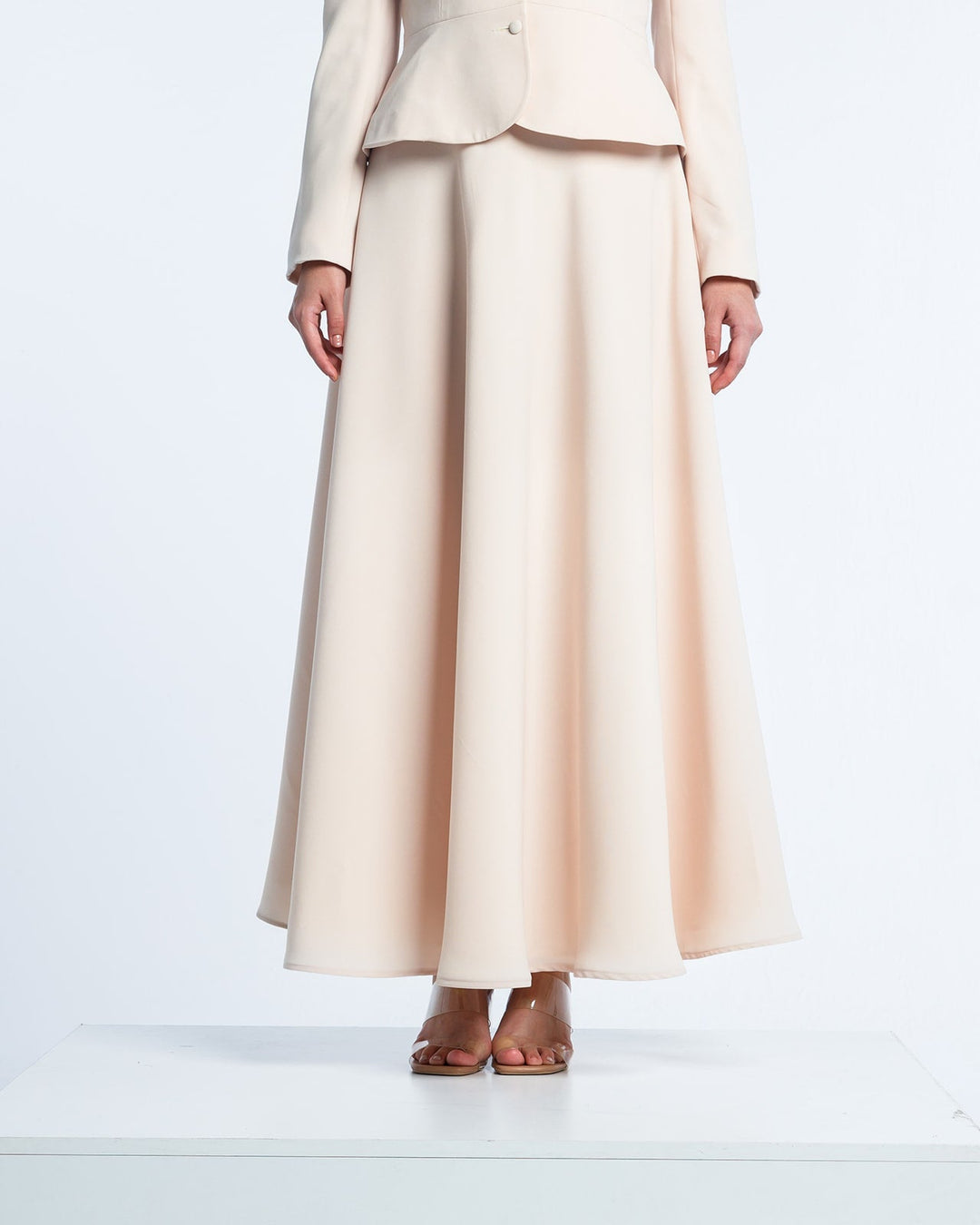 Elegant beige long sleeve suit with flared maxi skirt and nude heels on white background