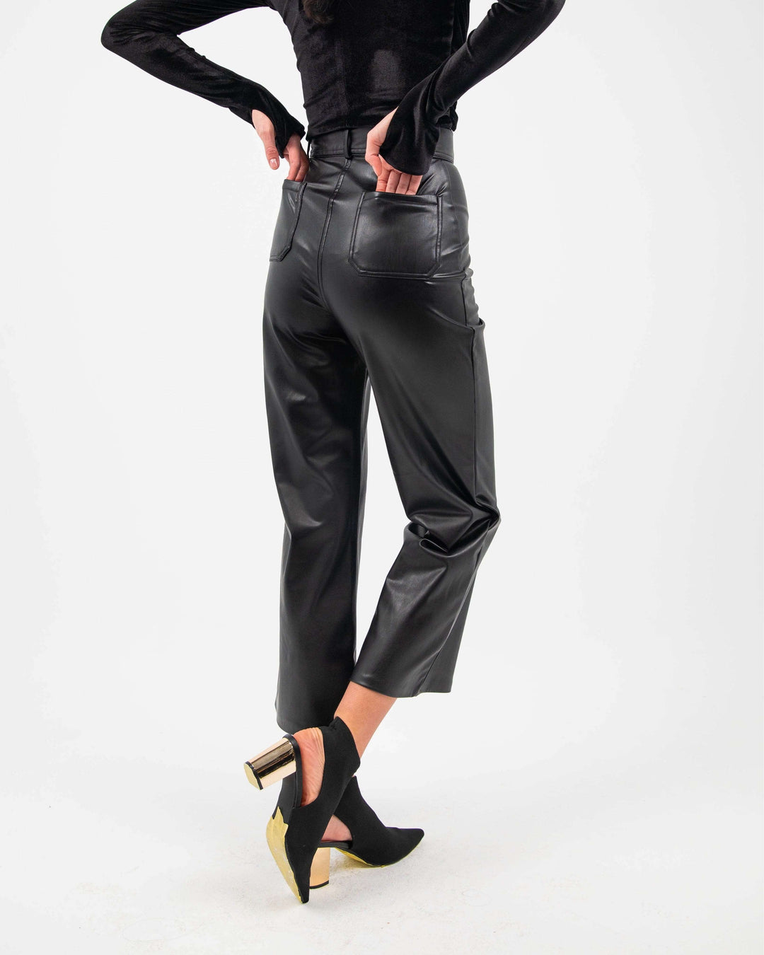 Woman wearing black straight leg faux leather pants with high heels on white background