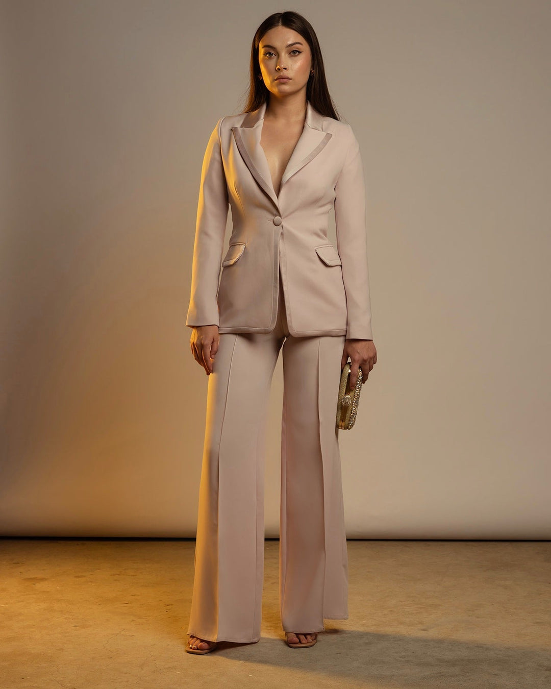 Woman wearing a cream-colored tailored suit with flared pants and holding a clutch bag
