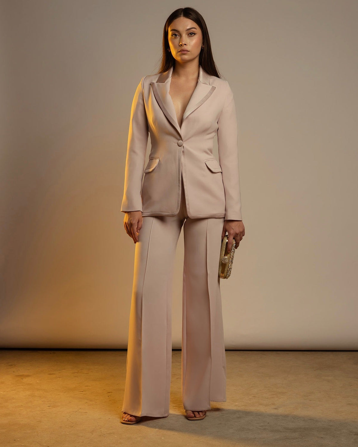 Woman wearing a cream-colored tailored suit with flared pants and holding a clutch bag
