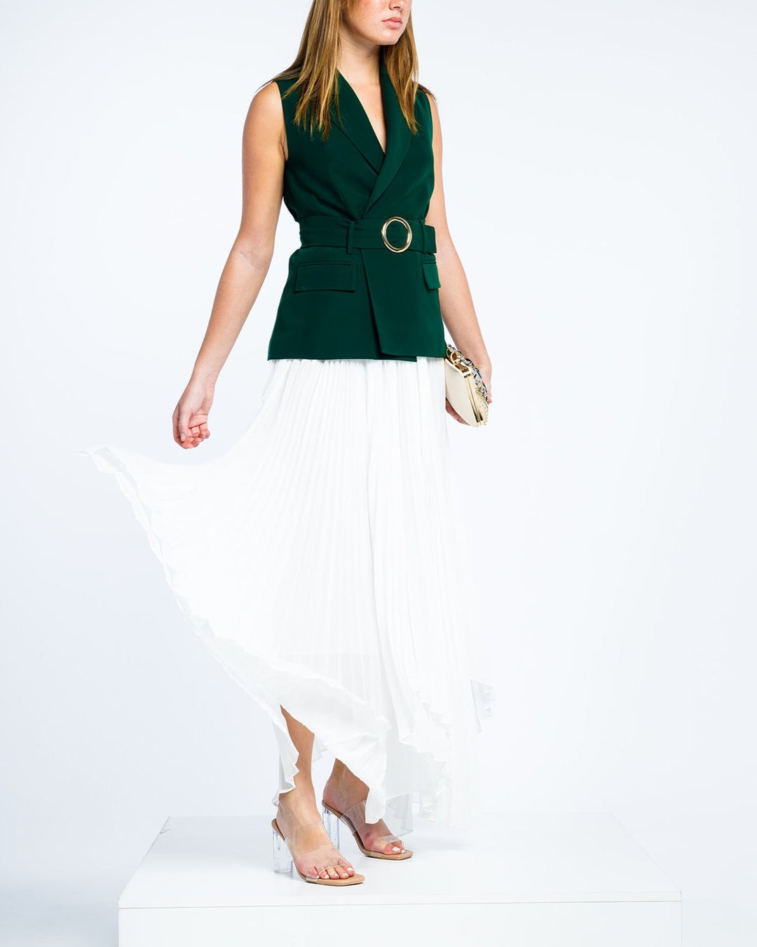 Woman wearing a sleeveless dark green belted blazer and white pleated maxi skirt