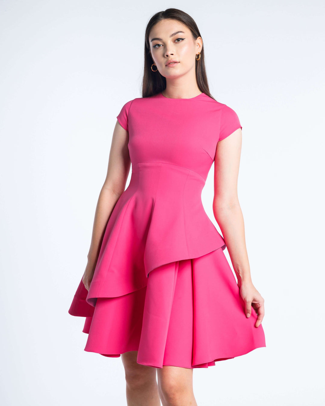 Woman wearing a short fuchsia layered dress with cap sleeves on a white background