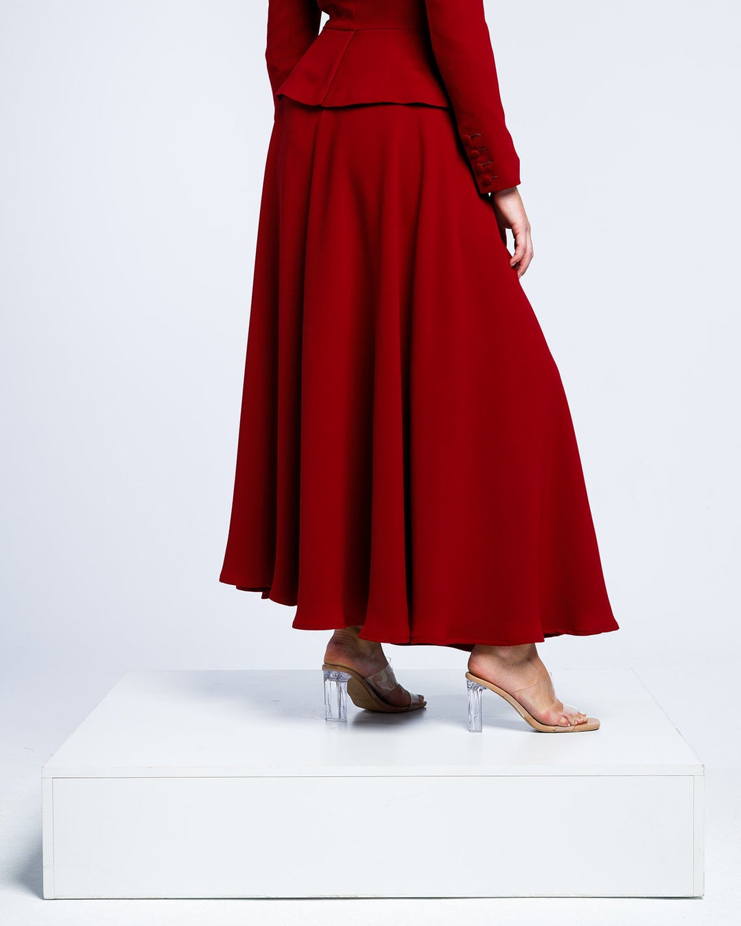 Woman wearing elegant long red dress with clear high-heel sandals on white platform
