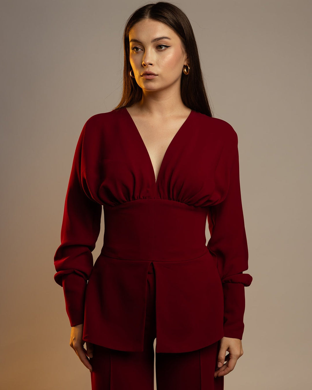 Woman wearing elegant deep red long-sleeve blouse with V-neck and tailored waist.