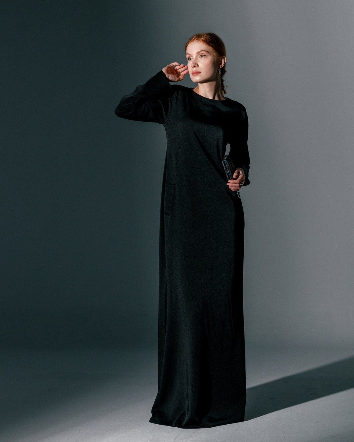 Woman wearing long black formal gown dress in minimal studio setting