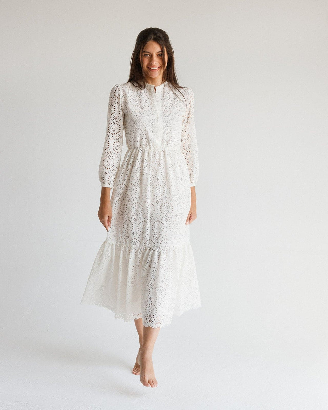 Woman in long sleeve white lace midi dress with floral eyelet pattern, standing barefoot