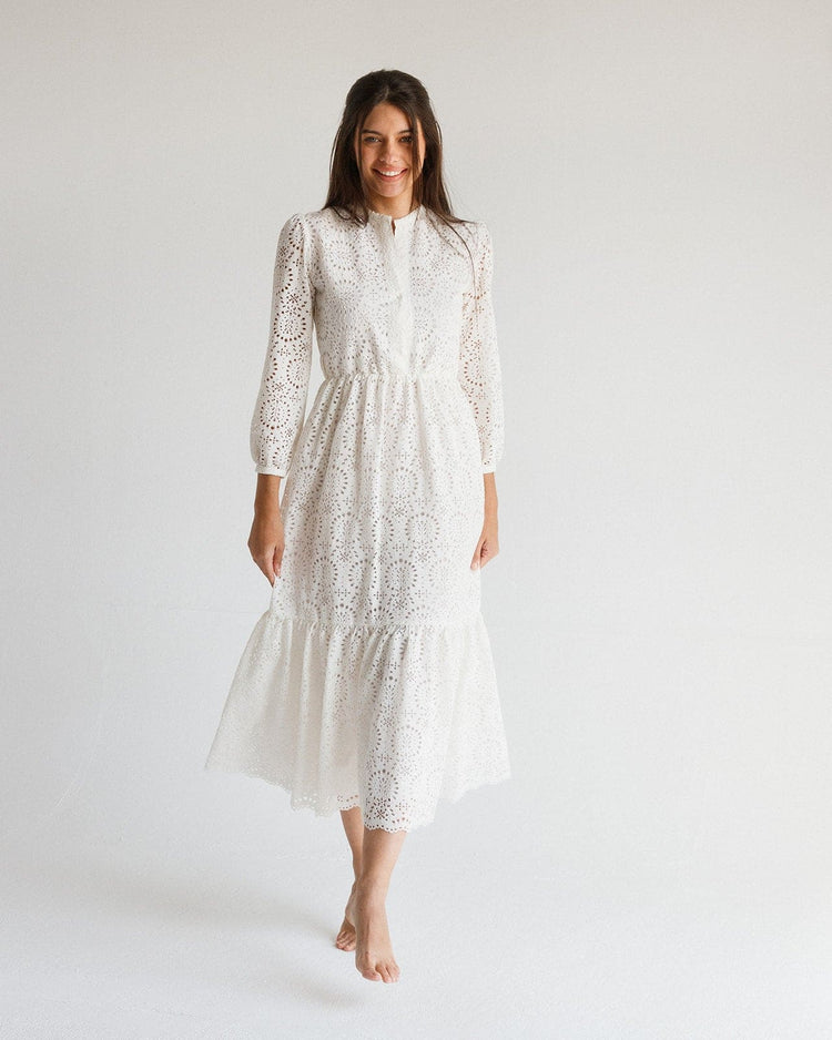 Woman in long sleeve white lace midi dress with floral eyelet pattern, standing barefoot