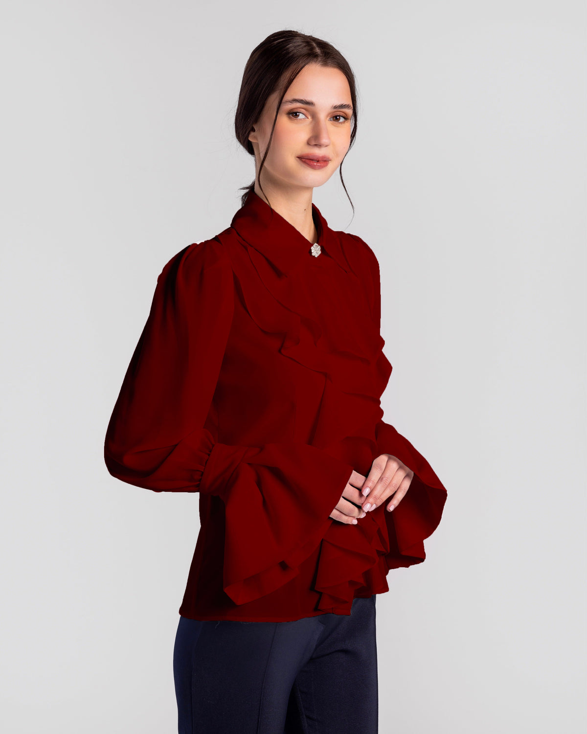 Woman in elegant long-sleeve ruffled red blouse with flared cuffs, posing indoors