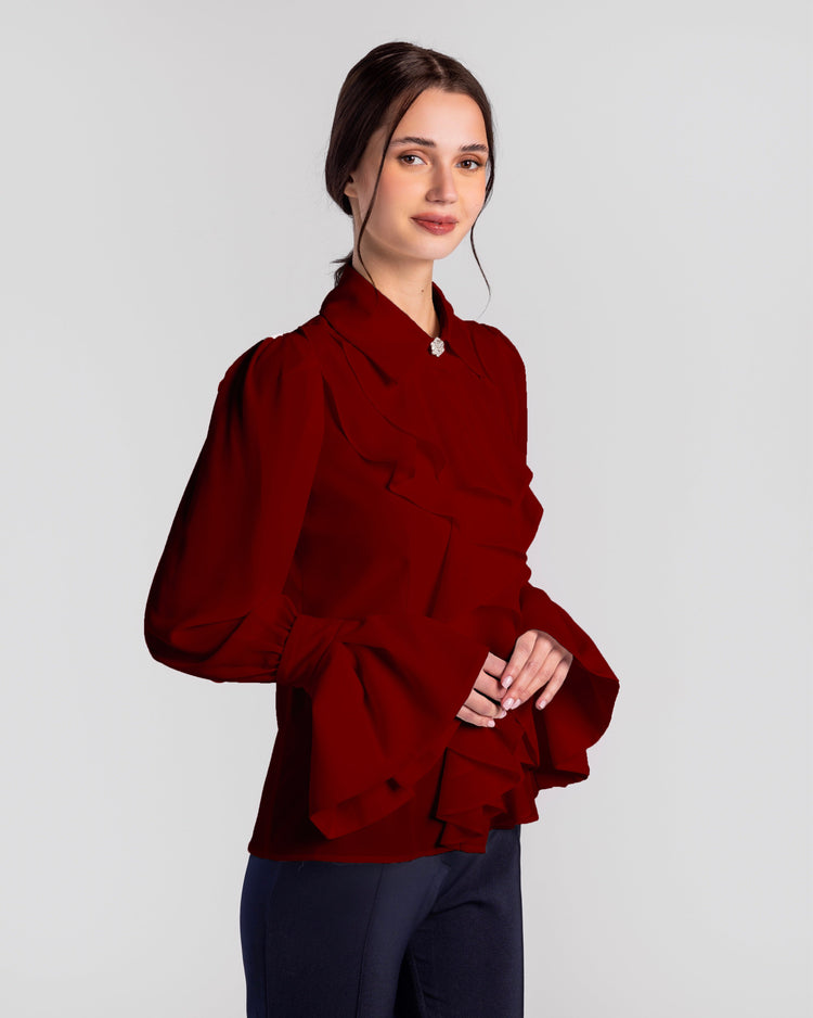 Woman in elegant long-sleeve ruffled red blouse with flared cuffs, posing indoors