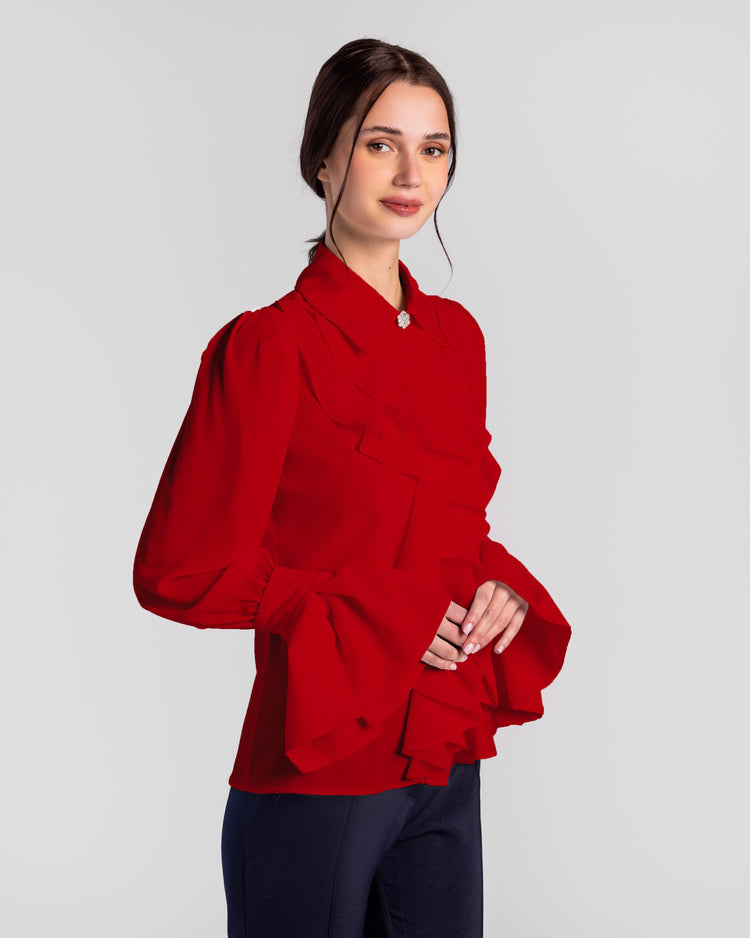 Woman wearing elegant red ruffled blouse with flared sleeves and black pants, studio setting