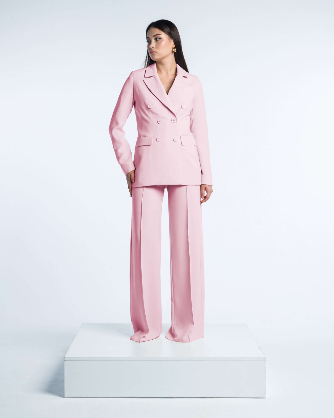 Woman wearing elegant pink double-breasted suit with wide-leg trousers on white platform