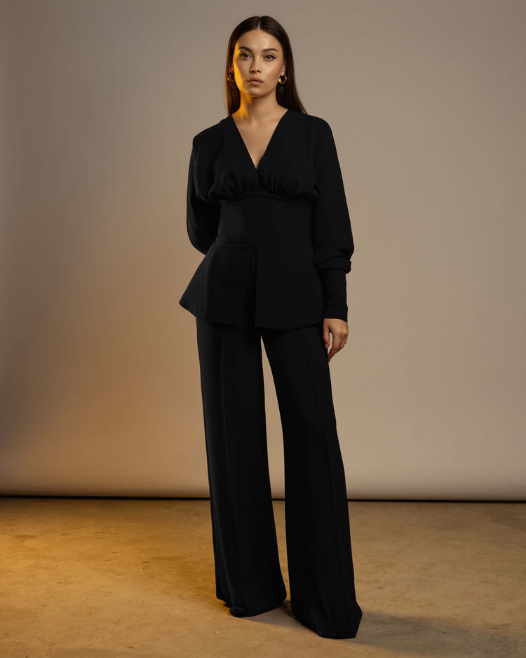 Woman wearing black wide-leg suit with fitted peplum top, elegant fashion studio shot