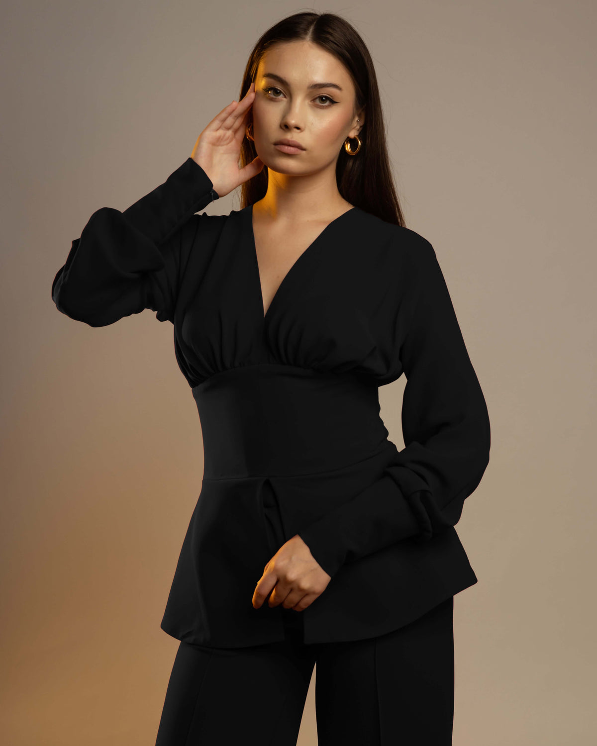 Woman wearing elegant black long-sleeve v-neck peplum top with gold hoop earrings