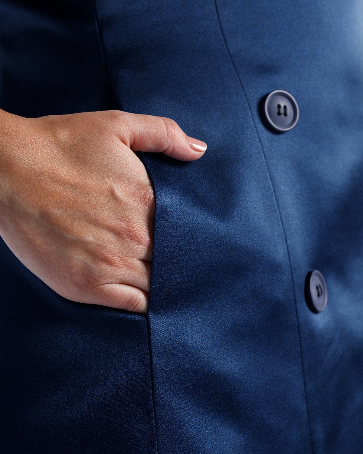 Close-up of a woman's hand in the pocket of a blue buttoned satin dress