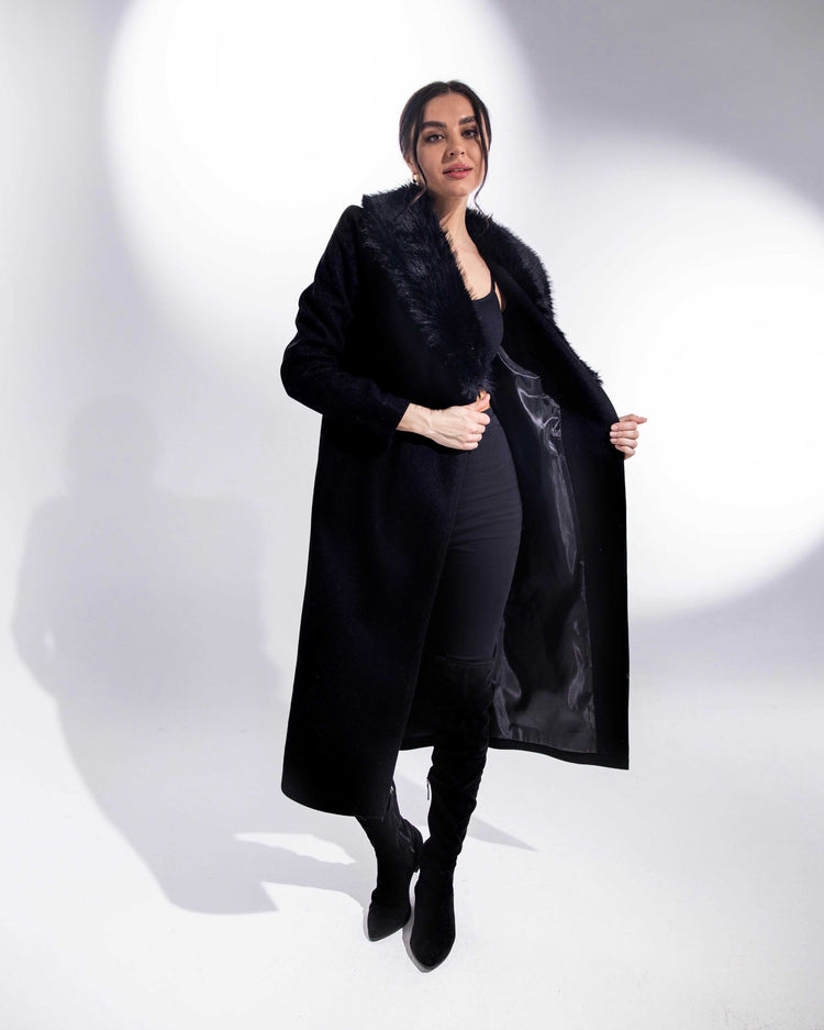 Woman modeling elegant black faux fur collar coat with thigh-high boots in studio