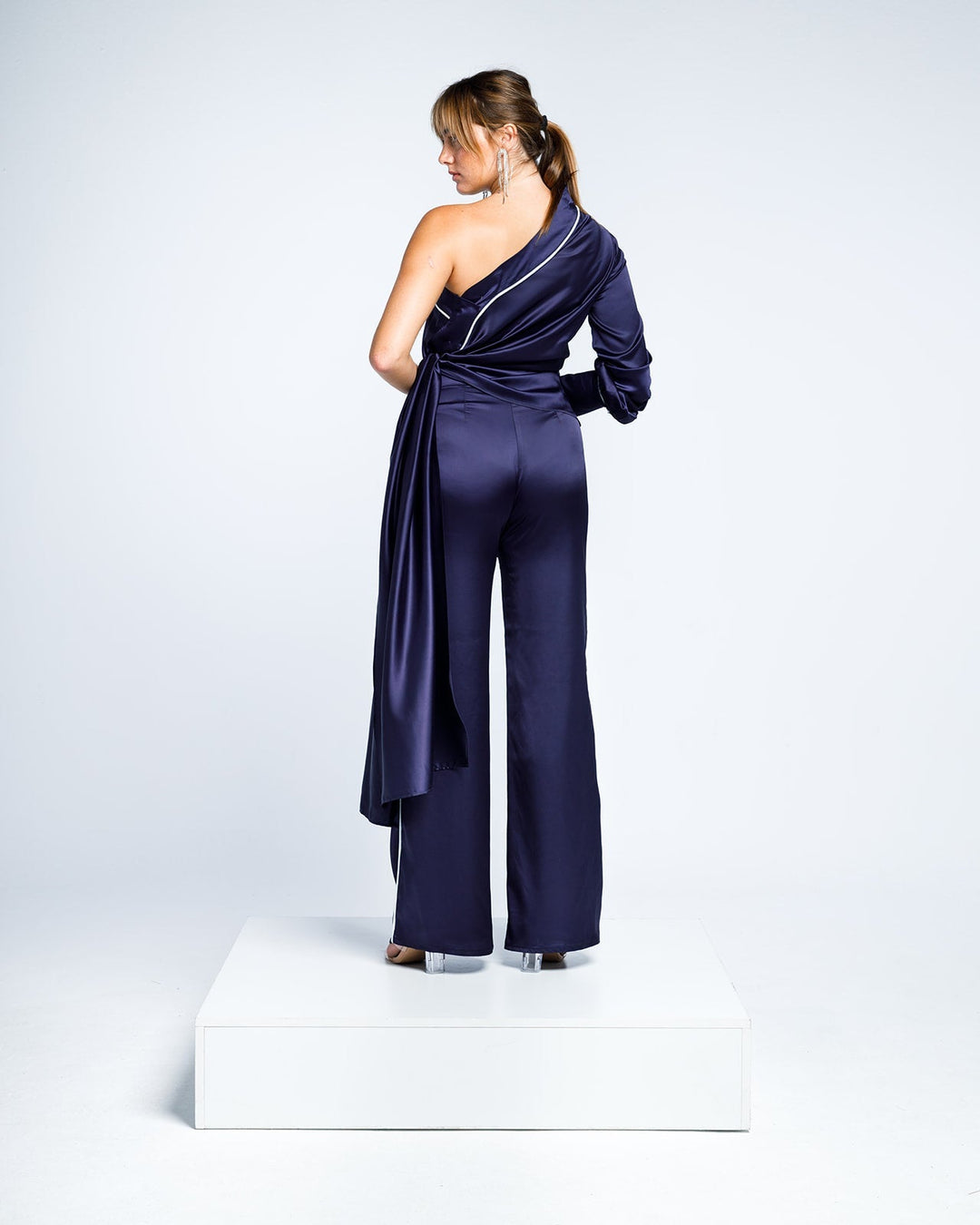 Woman modeling elegant navy blue satin one-shoulder jumpsuit with wide-leg pants