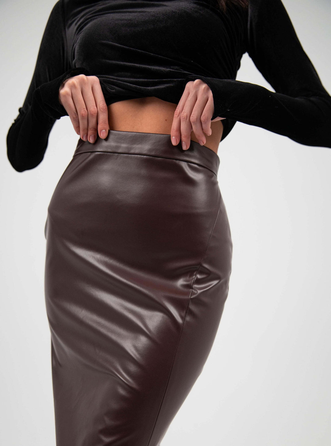 Woman wearing a high-waisted brown faux leather pencil skirt and black velvet top