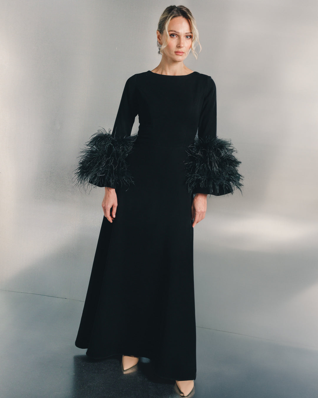 Woman in a long black evening dress with feathered sleeves and nude heels