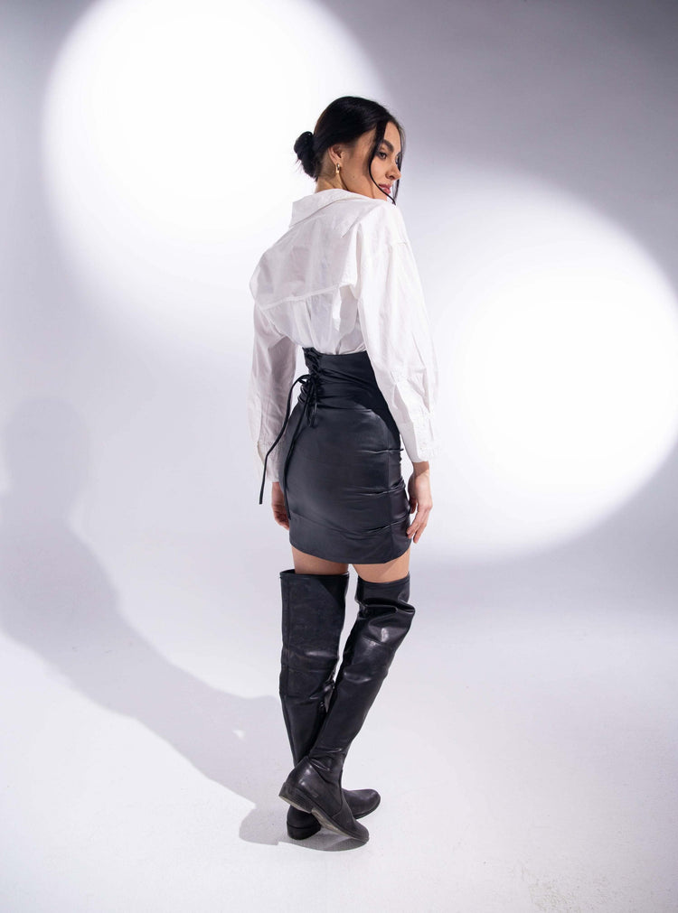 Woman wearing white blouse, black leather mini skirt, and thigh-high boots in studio