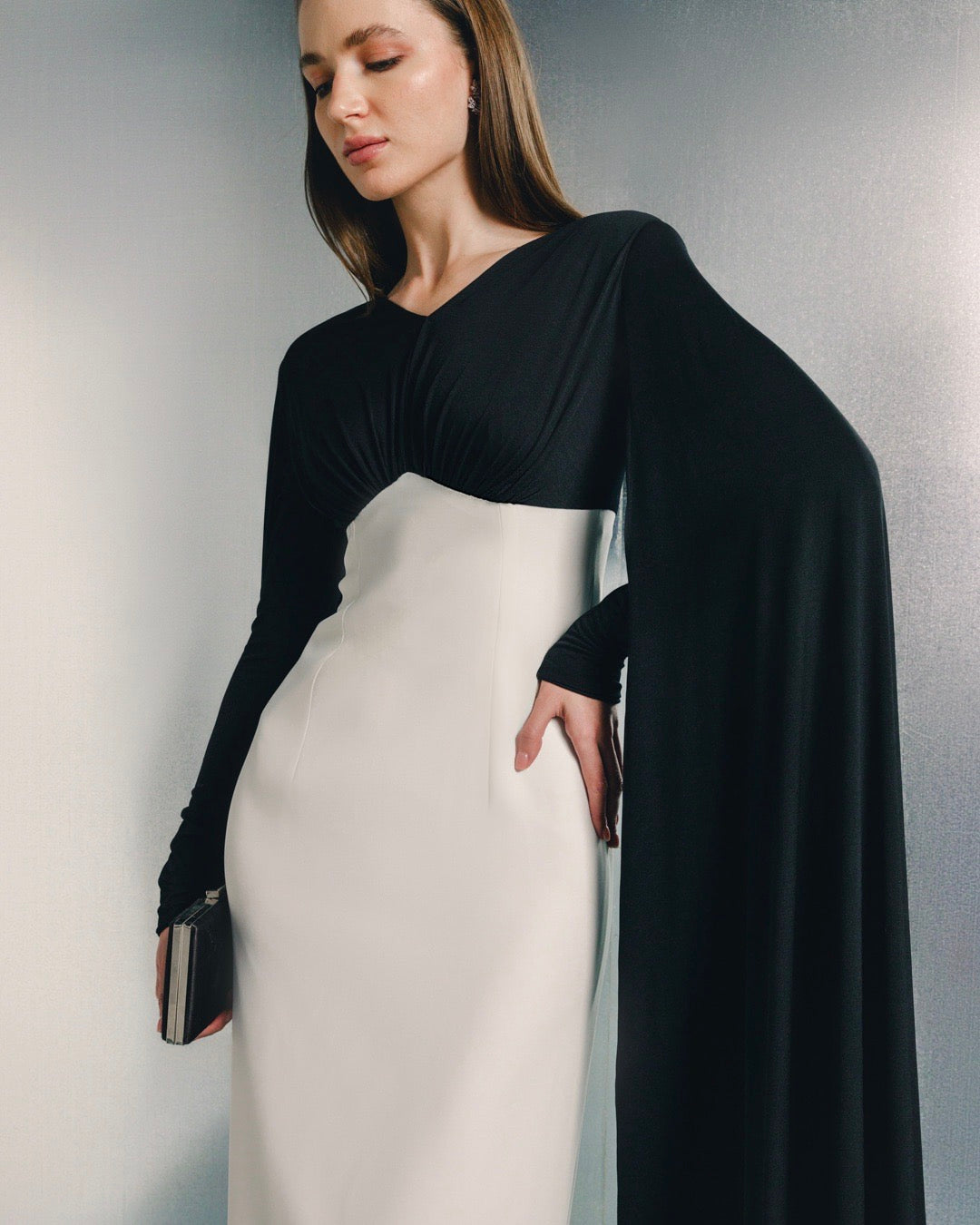 Elegant woman in a black and white gown with long sleeve detail, holding a clutch