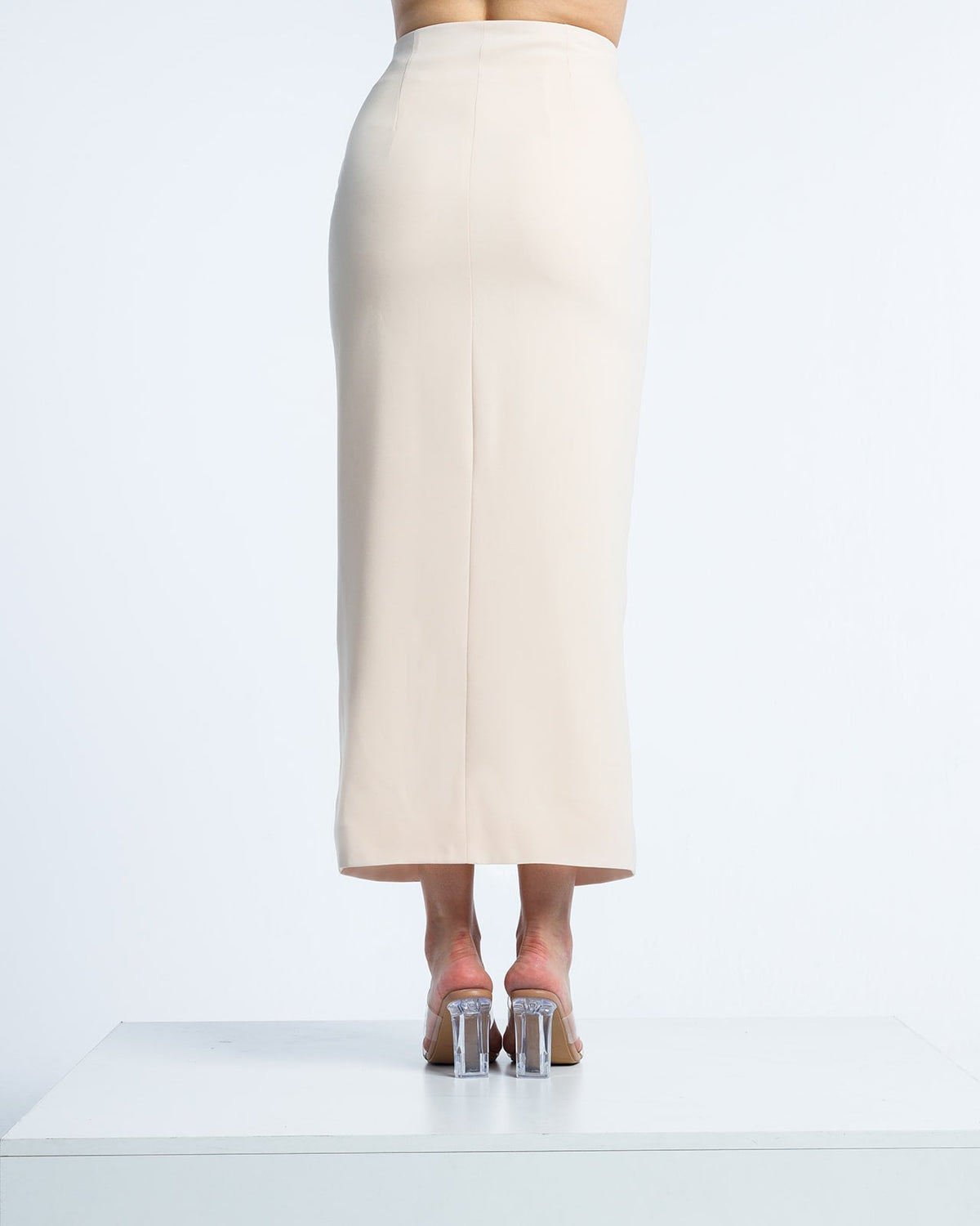 Back view of woman in high-waisted beige midi pencil skirt and clear block heels
