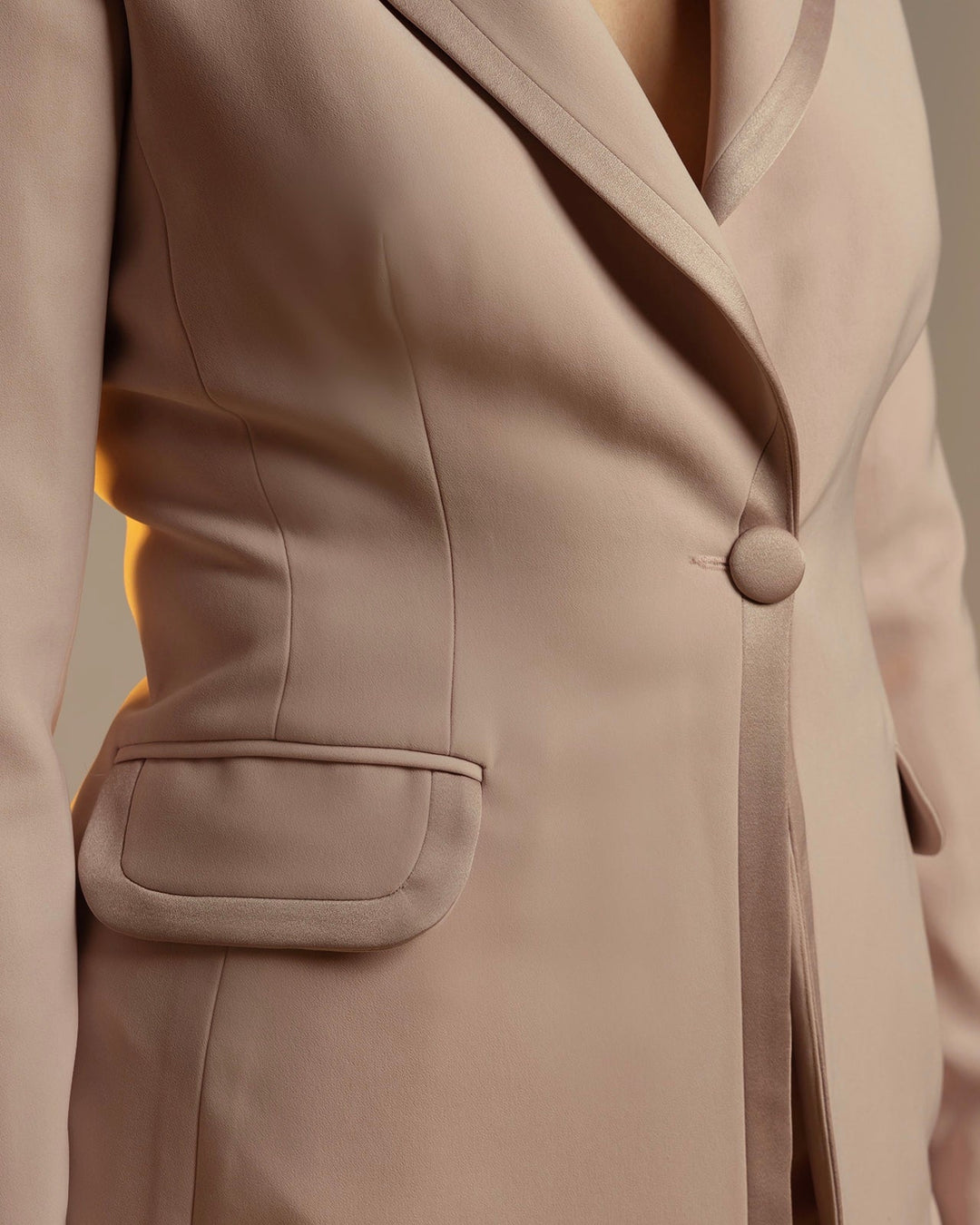 Close-up of a tailored women's beige blazer with satin lapel and button detail