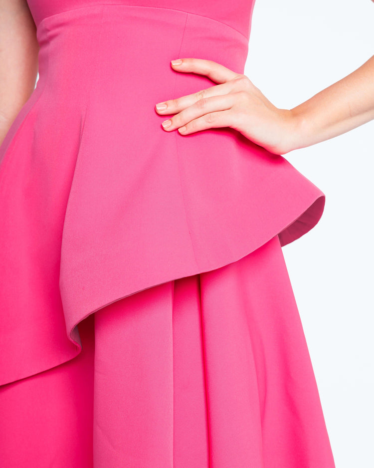 Woman wearing vibrant fuchsia pink dress with structured peplum and hand on hip