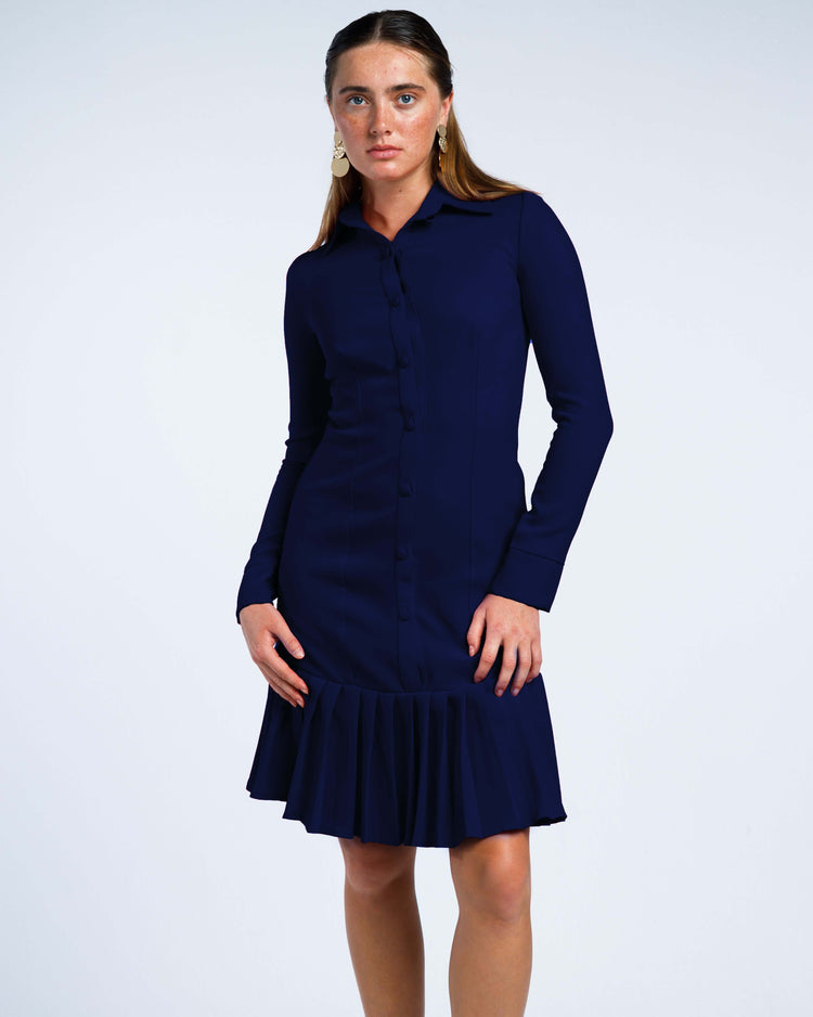 Woman wearing a navy blue long sleeve collared dress with pleated hem against white background
