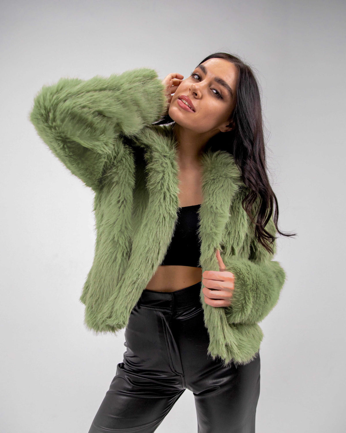 Woman wearing olive green faux fur jacket with black crop top and leather pants