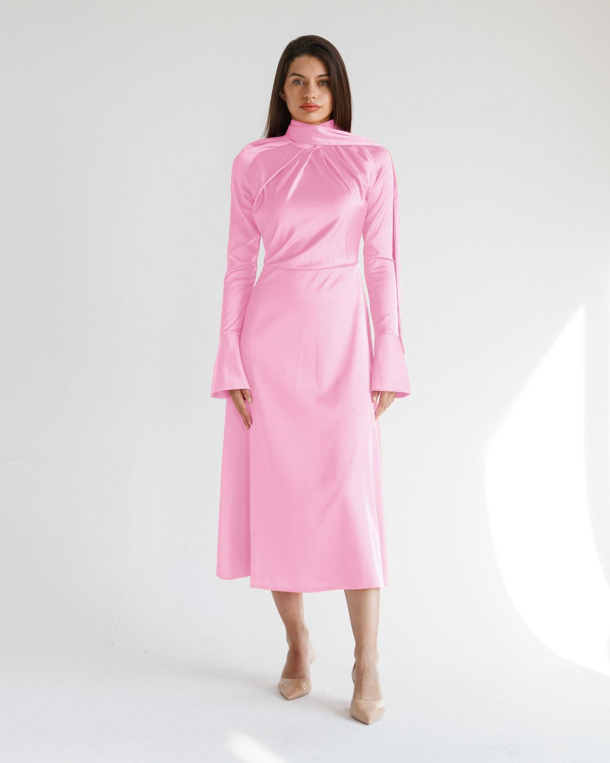 Woman modeling elegant long sleeve pink satin midi dress with high neck