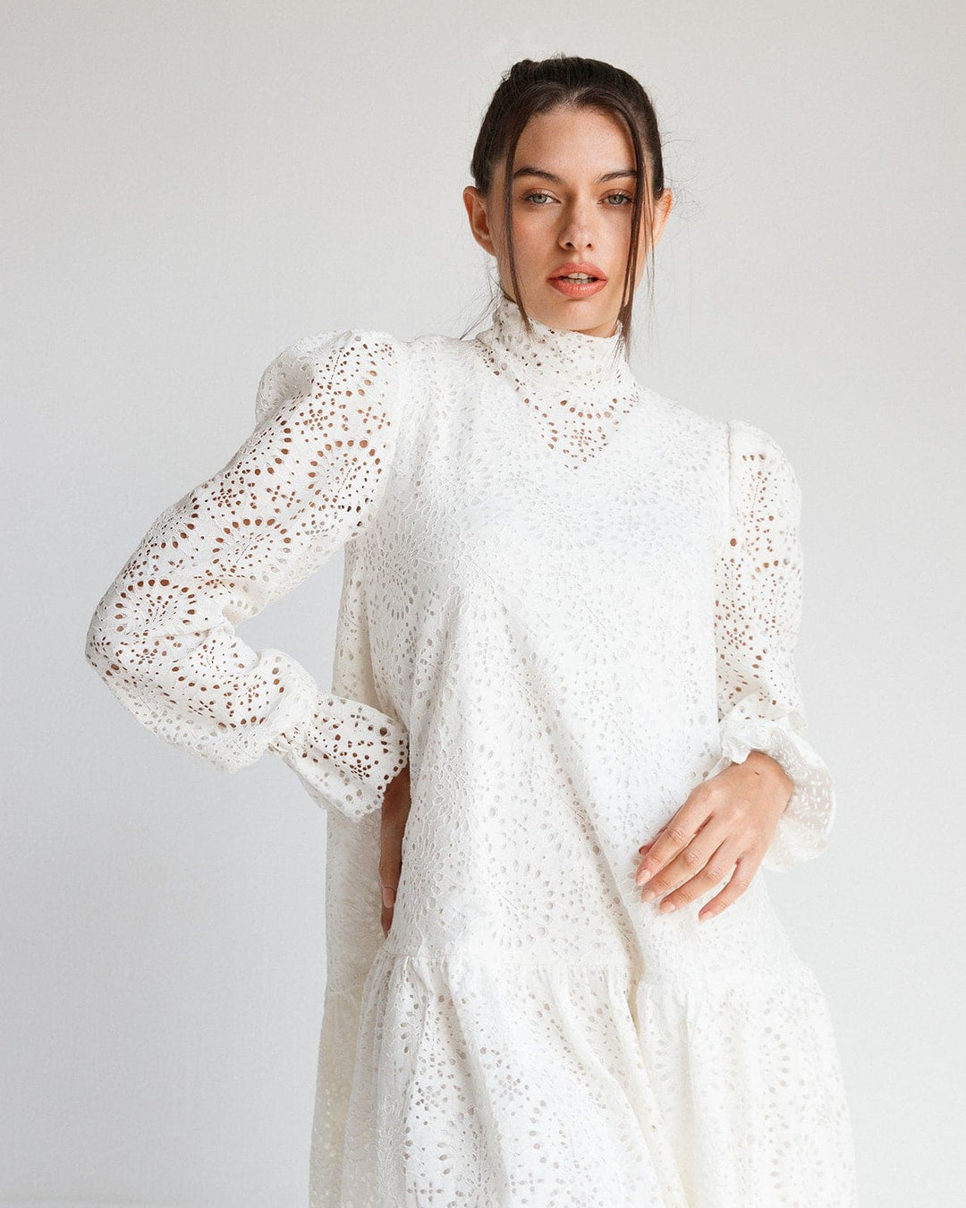 Woman wearing a white lace eyelet long-sleeve dress with high neck and puffed shoulders.