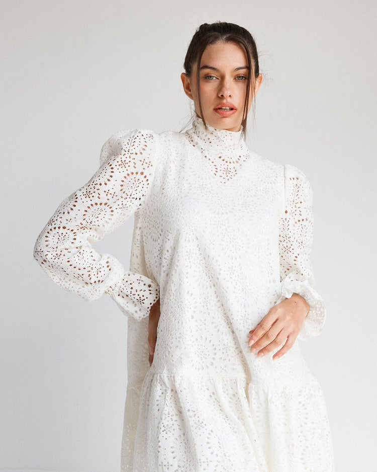 Woman wearing a white lace eyelet long-sleeve dress with high neck and puffed shoulders.