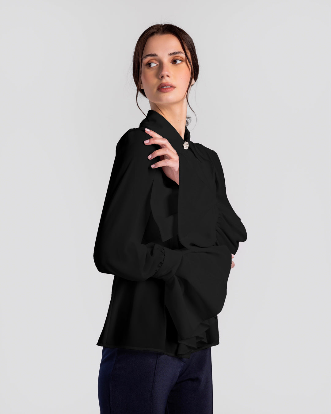 Woman wearing elegant black long sleeve blouse with large bow collar and wide cuff sleeves.