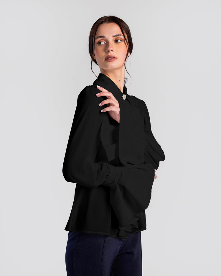 Woman wearing elegant black long sleeve blouse with large bow collar and wide cuff sleeves.