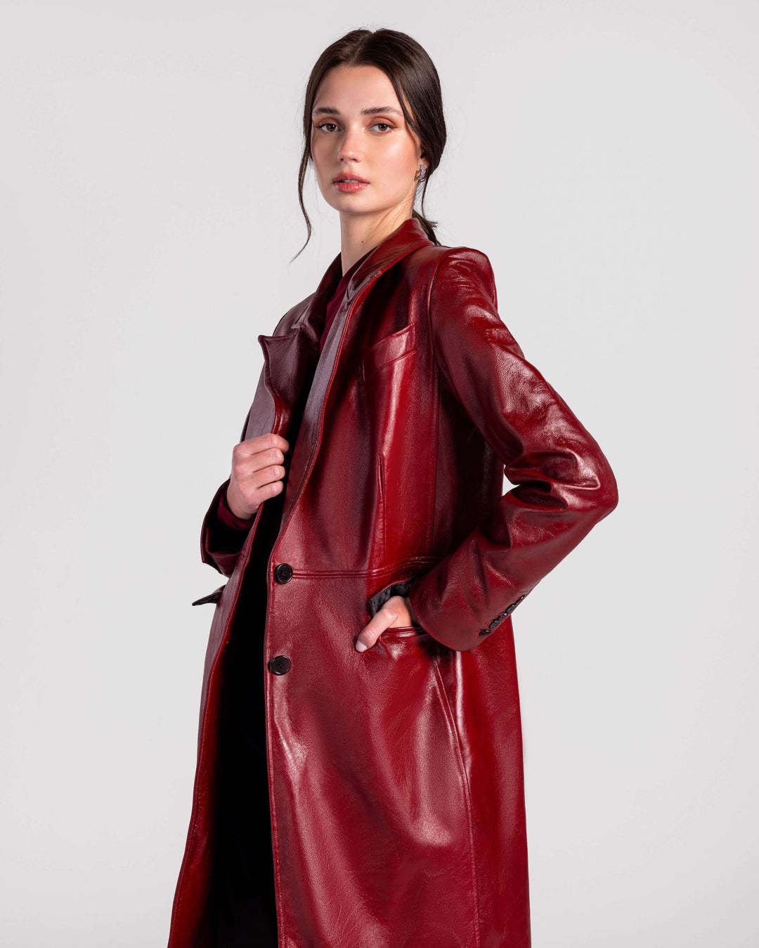 Woman wearing a long, glossy red leather coat with black buttons, posing stylishly.