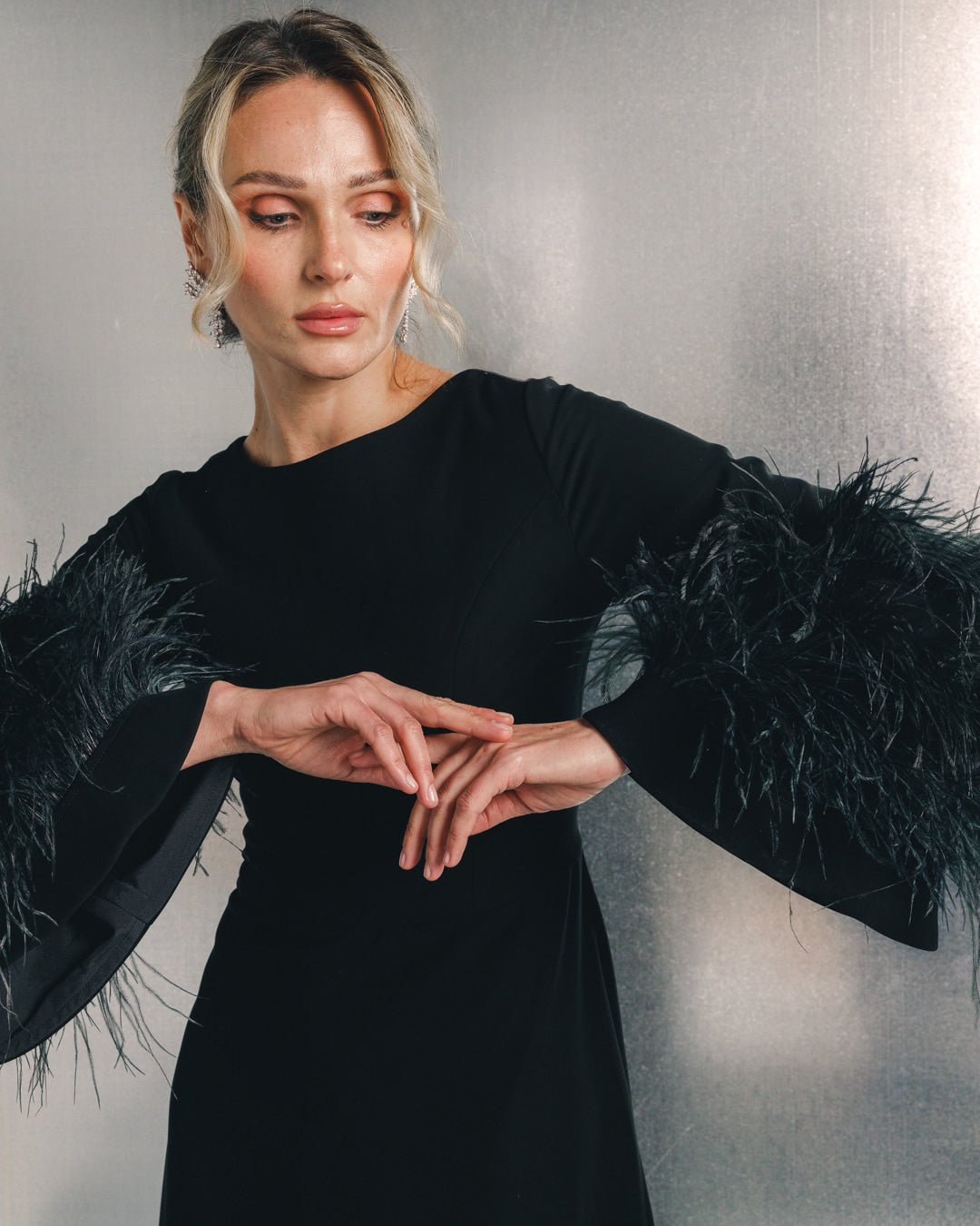 Woman in elegant black dress with dramatic feathered sleeves, fashion photoshoot setting