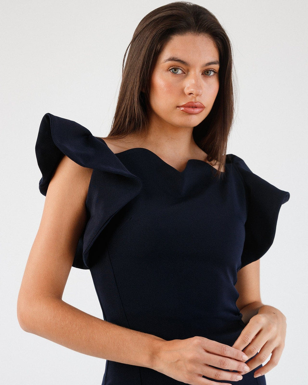 Woman wearing elegant dark blue dress with structured ruffle sleeves, posing indoors