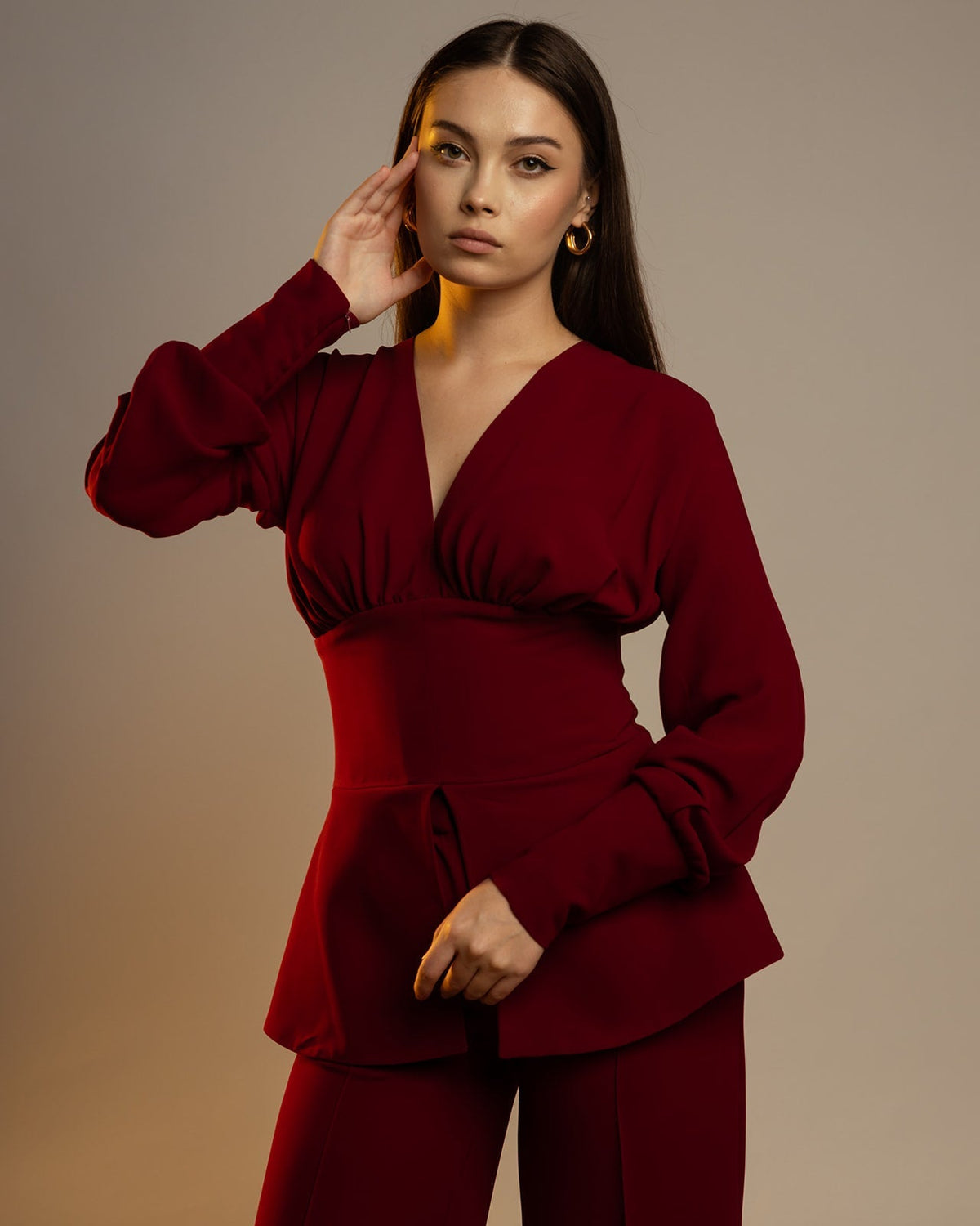 Woman modeling elegant burgundy suit with long sleeves and wide-leg pants, neutral background