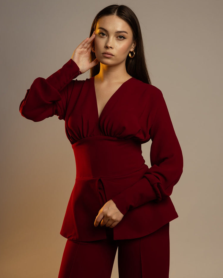 Woman modeling elegant burgundy suit with long sleeves and wide-leg pants, neutral background